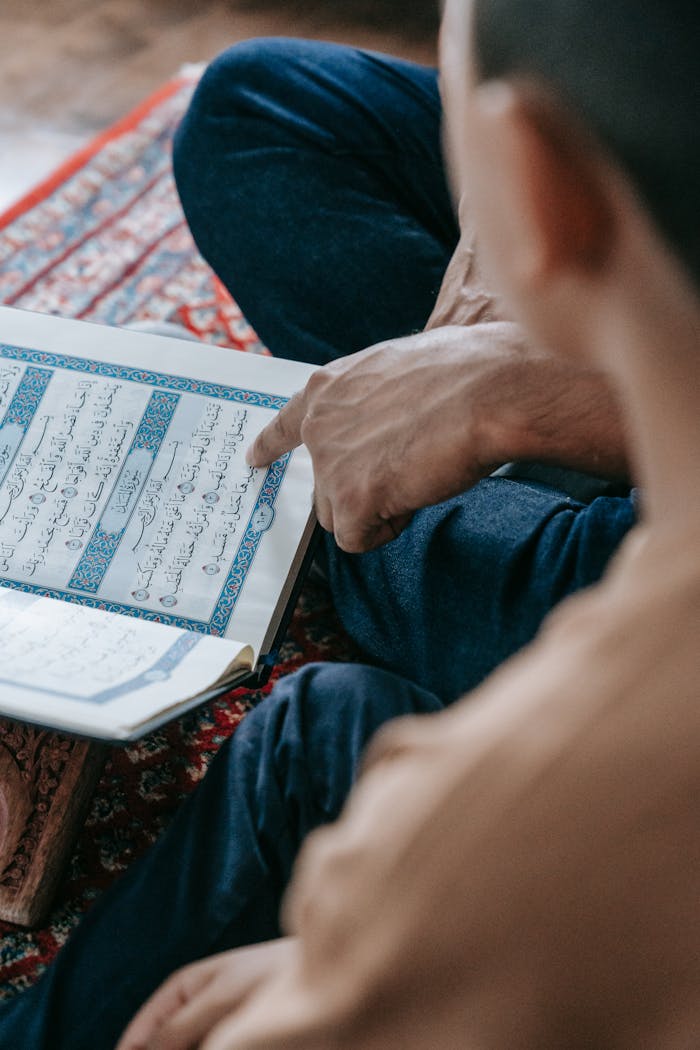 An adult points to Arabic text during study indoors.